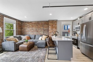 Ein modernes Wohnzimmer mit einem grauen Sofa, einem Couchtisch und einem gemusterten Teppich.
