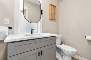 A bathroom with a white sink, a mirror, a toilet, and a towel rack. - Historic Brownstone Apartment, Heirloom Vacations (Duluth)
