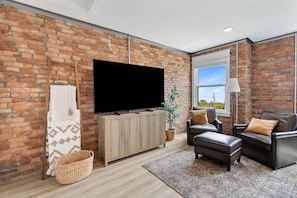 Ein Wohnzimmer mit Backsteinwand, Flachbildfernseher, Holzschrank, Ledersofas und einem großen Fenster.