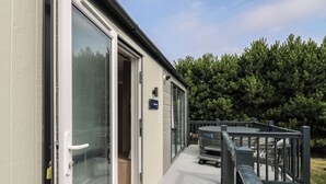 A modern building with a glass door entrance, a deck area with outdoor seating, and a sign indicating the name of the property.