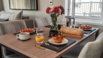 A dining table with breakfast items, a vase with flowers, and a view of the outside.