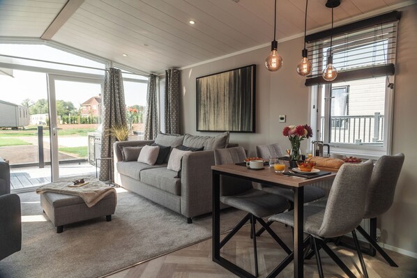 A modern living room with a sofa, a dining table with chairs, a coffee table, and a large window with curtains.
