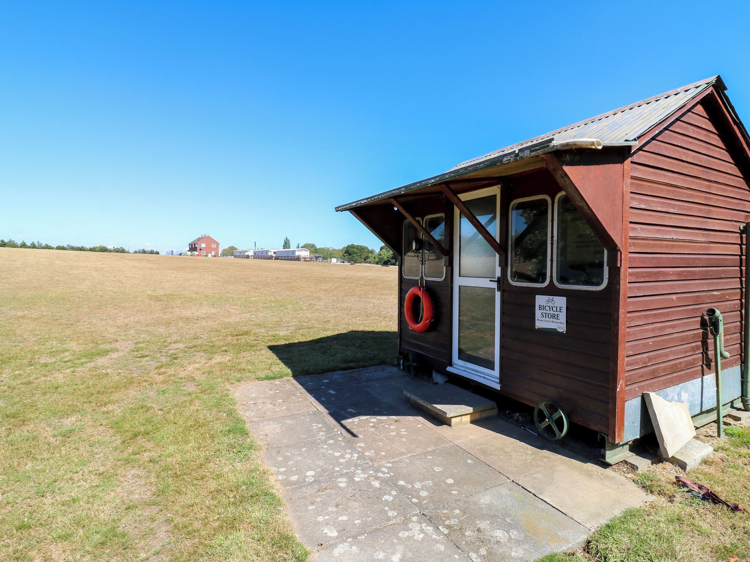 A small wooden building with a sign indicating a bicycle store, a lifebuoy hanging on the door, and a clear sky in the background.