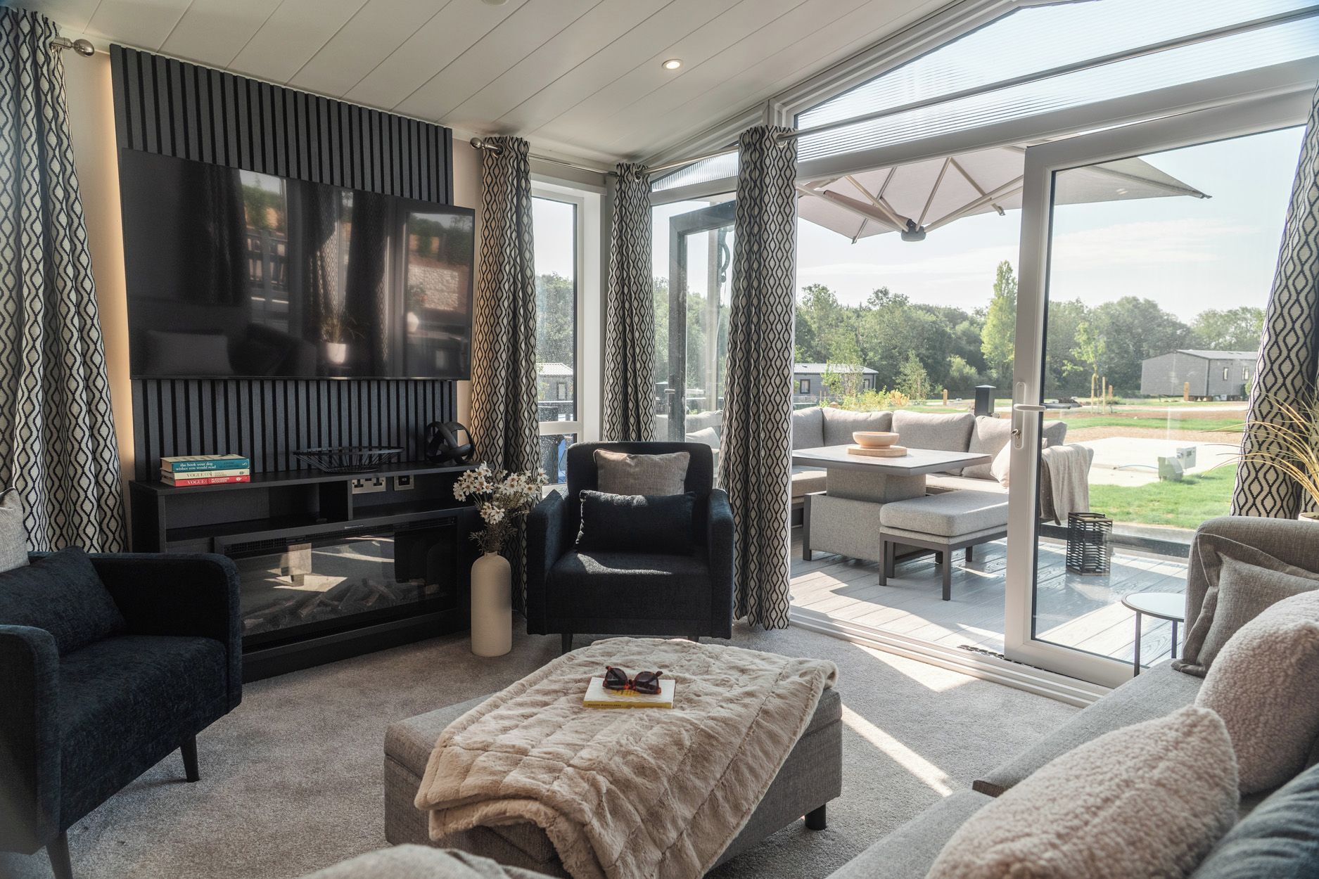 A modern living room with a flat-screen TV, comfortable seating, and a glass door leading to an outdoor patio.
