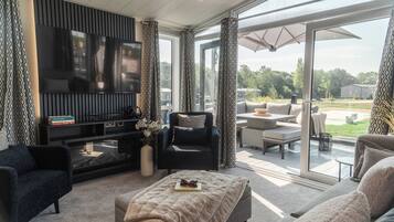 A modern living room with a flat-screen TV, comfortable seating, and a glass door leading to an outdoor patio.