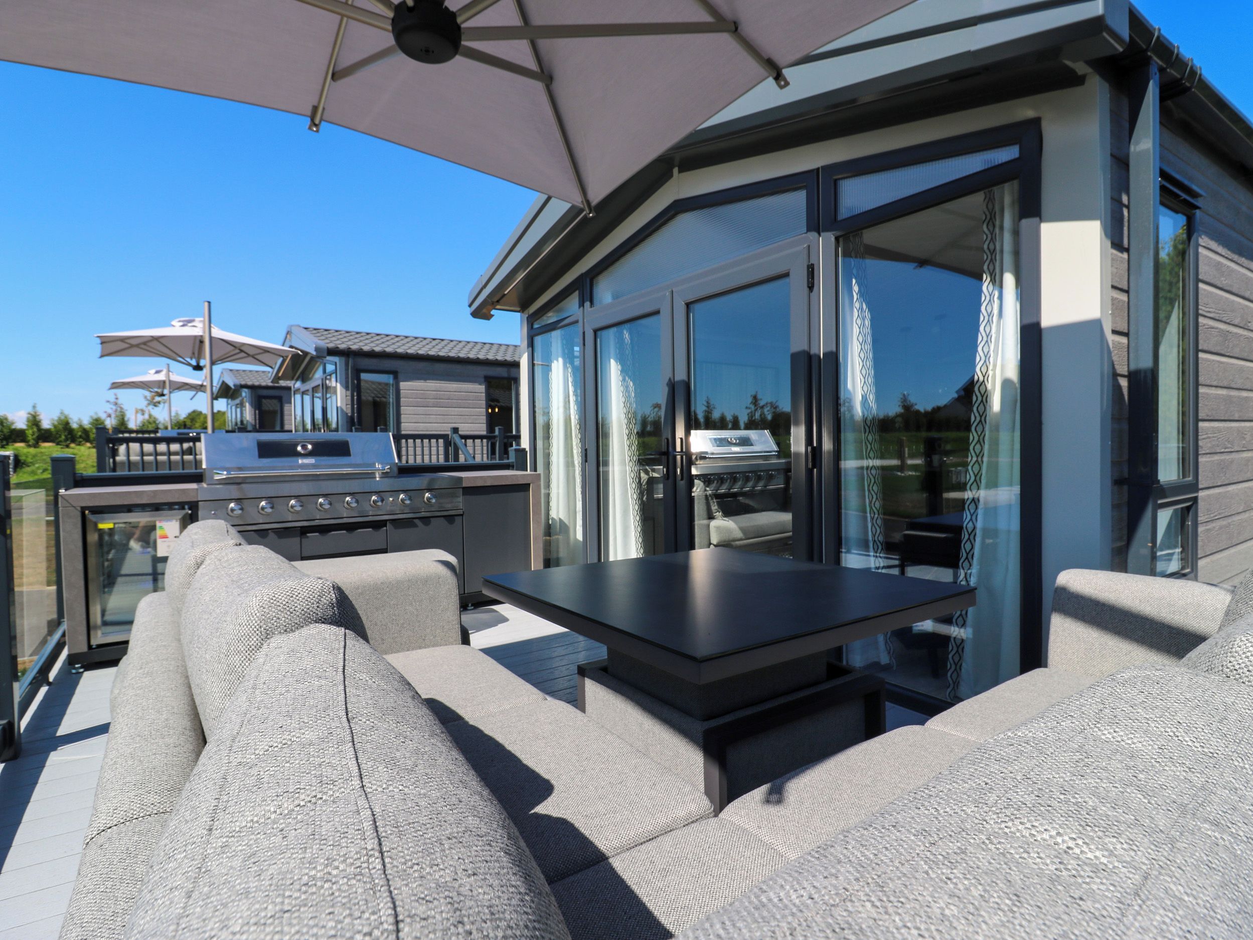 Un patio exterior con una parrilla, zona de estar y ventanas amplias.