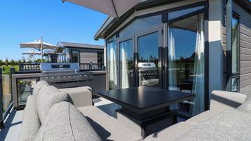An outdoor patio with a grill, seating area, and large windows.