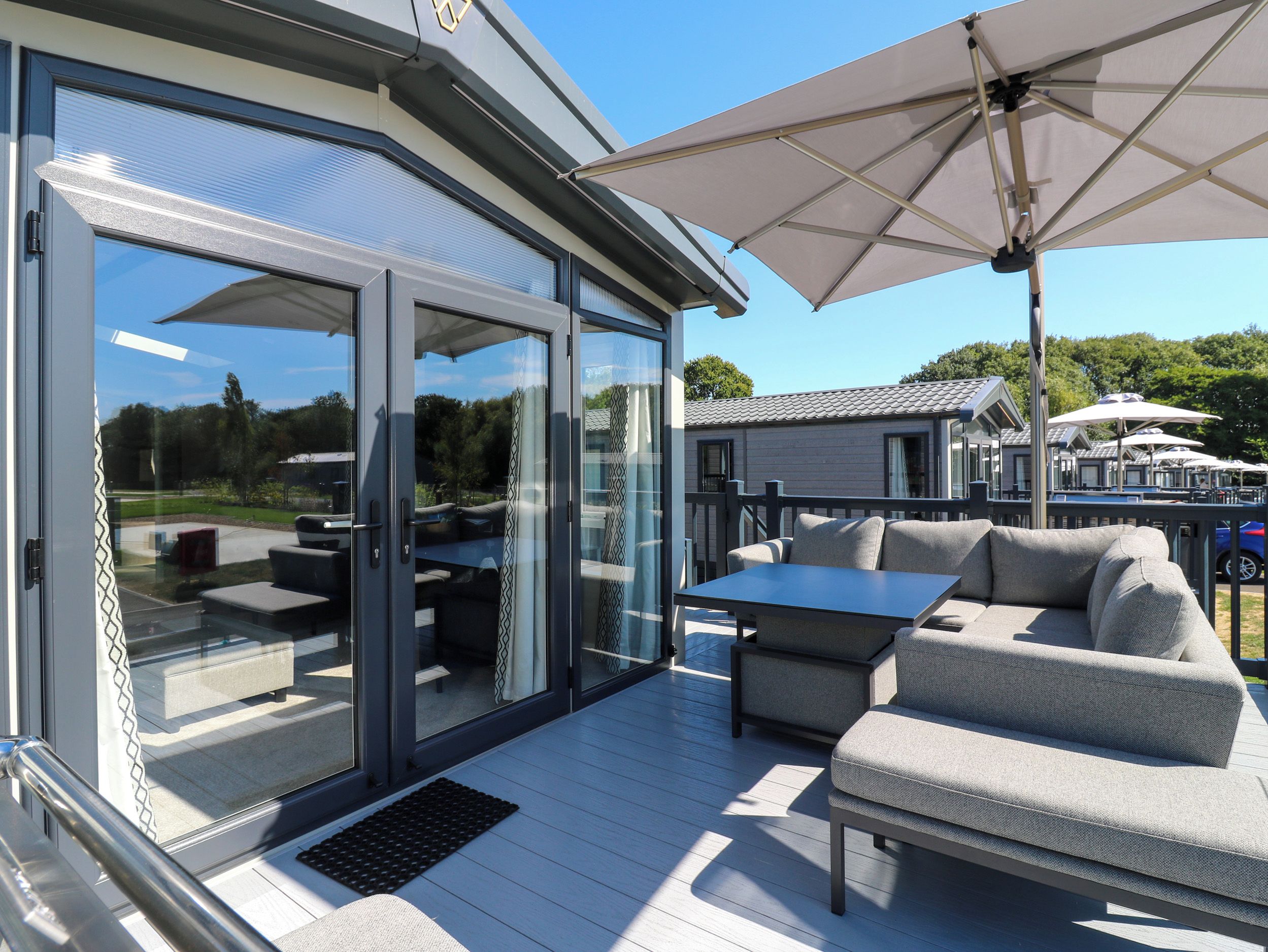 Una terraza con mobiliario exterior, una puerta de cristal y un gran paraguas.