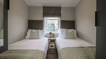 A twin room with two beds, a small table, a window with a view, and a ceiling light.