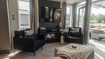 A modern living room with a flat-screen TV, two armchairs, a coffee table, and a fireplace.