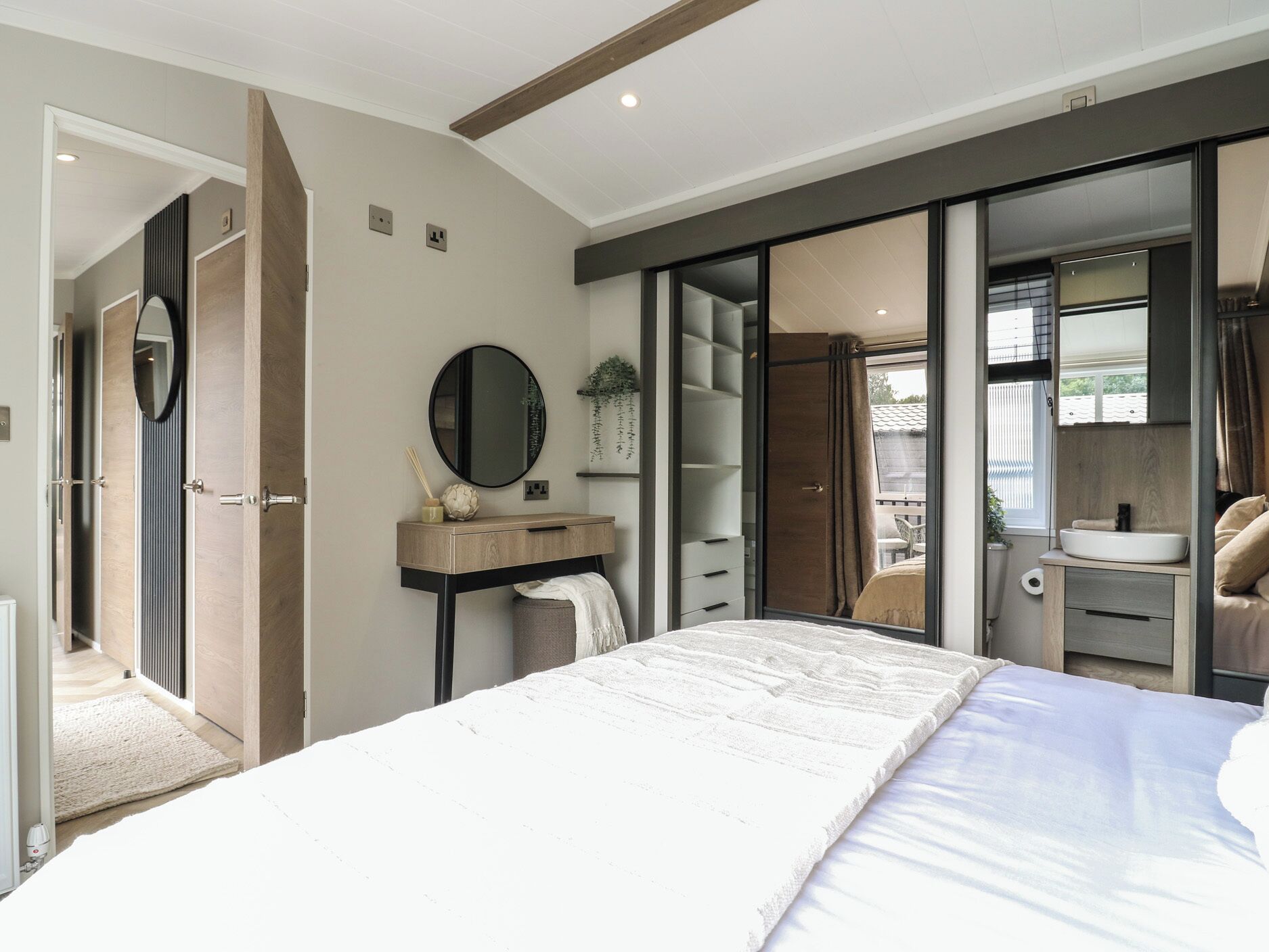 Un dormitorio moderno con una cama grande, una mesita de noche, un espejo y un armario con puertas correderas.