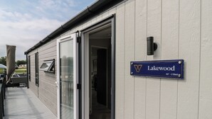 A building with a sliding glass door entrance, a sign indicating 'Lakewood 42' - 2 Bed', and a small outdoor seating area.