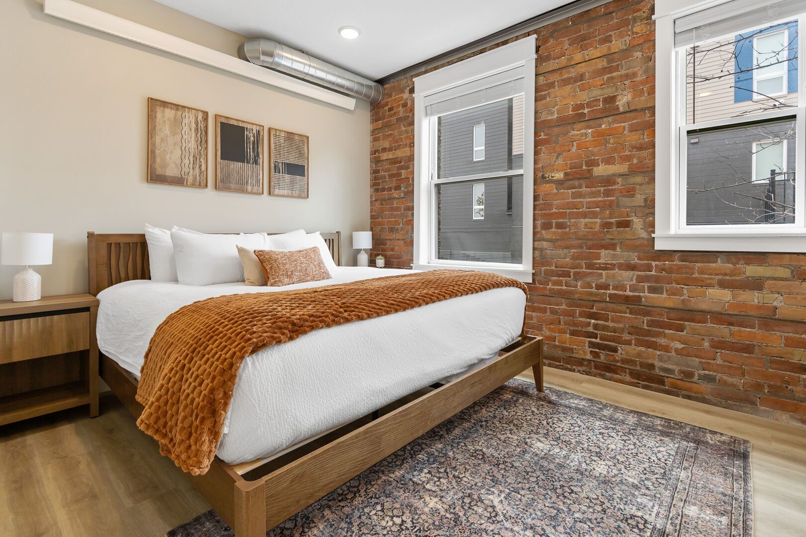 Un dormitorio con cama, mesitas de noche, una pared de ladrillo y una ventana.