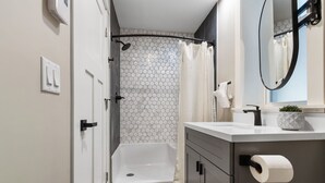 Et moderne badeværelse med bruser, toilet og håndvask med spejl.