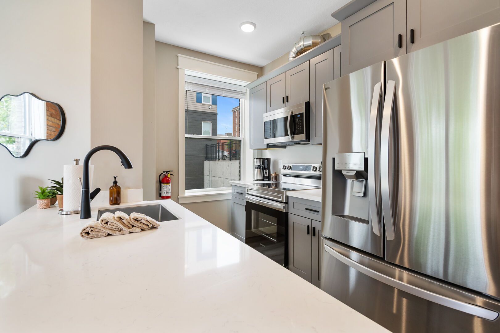 A modern kitchen with stainless steel appliances, a large island with a sink, and a window overlooking the street.