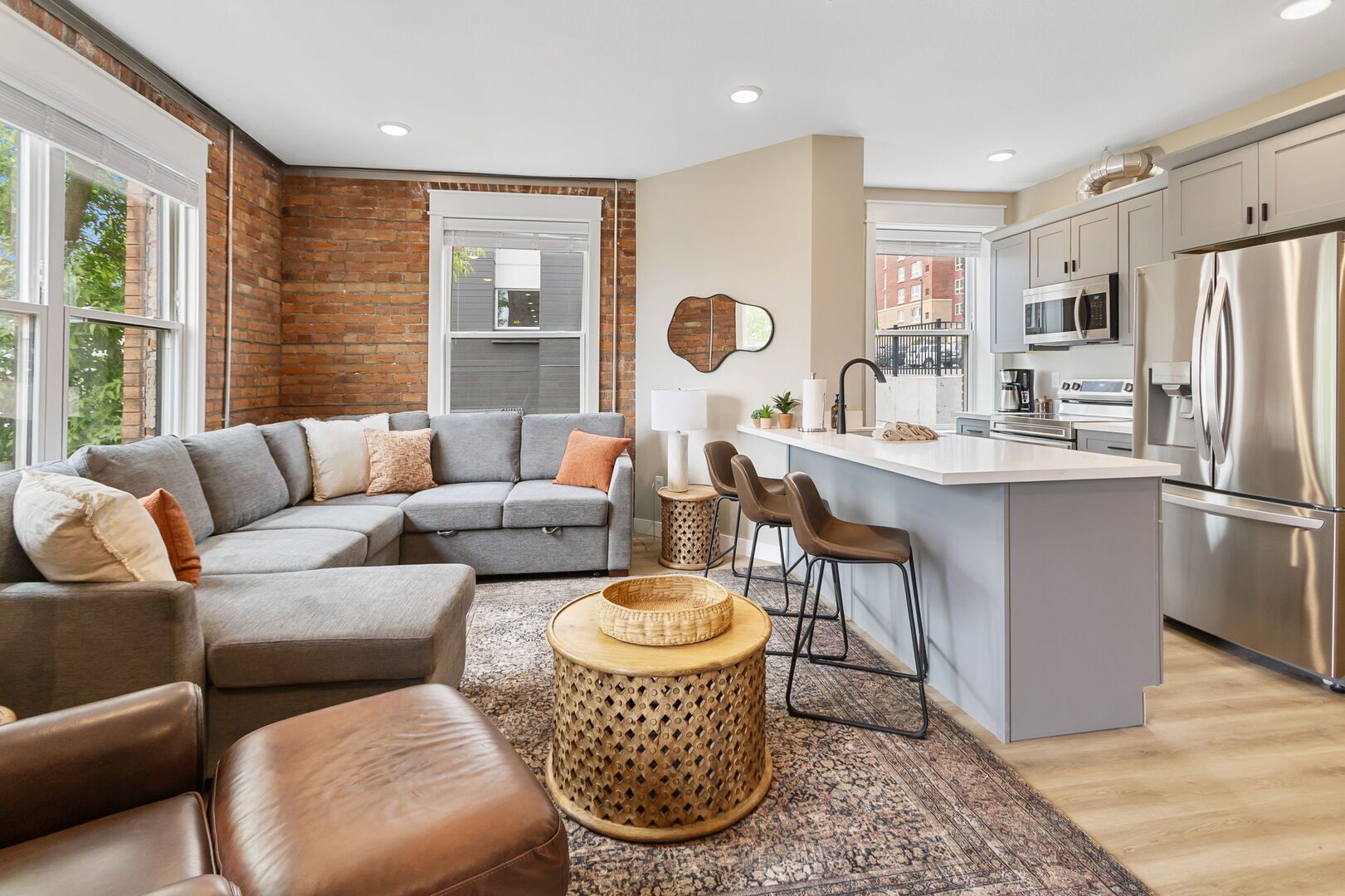 A modern kitchen with stainless steel appliances, a grey sofa, and a large window.