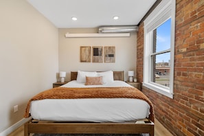 Ein Schlafzimmer mit einem Bett, einem Fenster, einer Ziegelwand und einem Deckenlüfter.