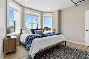 Ein Schlafzimmer mit einem Bett, Nachttischen, einem Fenster und einem gemusterten Teppich.