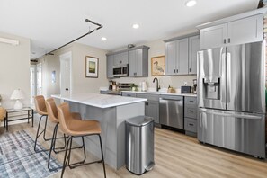 A modern kitchen with grey cabinets, stainless steel appliances, and a central island with bar stools. - Historic Brownstone Apartment, Heirloom Vacations (Duluth)