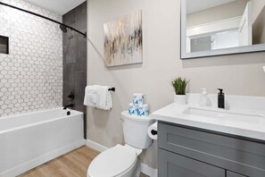 Ein modernes Badezimmer mit Wand aus sechseckigen Fliesen, einer Badewanne, einer Toilette und einem Waschtisch mit Spiegel.