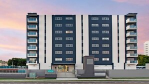 Ein mehrstöckiges Hotel mit modernem Design, das einen zentralen Eingang und Balkone in jeder Etage bietet.