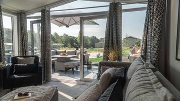 Ein modernes Wohnzimmer mit einer Couch, einem Sessel und einem Tisch. Ein Glastür führt zu einer Außenpatio-Terrasse.