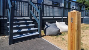 A building with a staircase leading to a deck area, a wooden post with a number, and a bench.