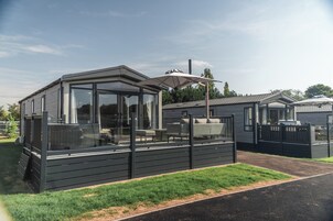 Una casa móvil moderna de un piso con un porche acristalado, una parrilla empotrada y una zona de estar cubierta al aire libre.
