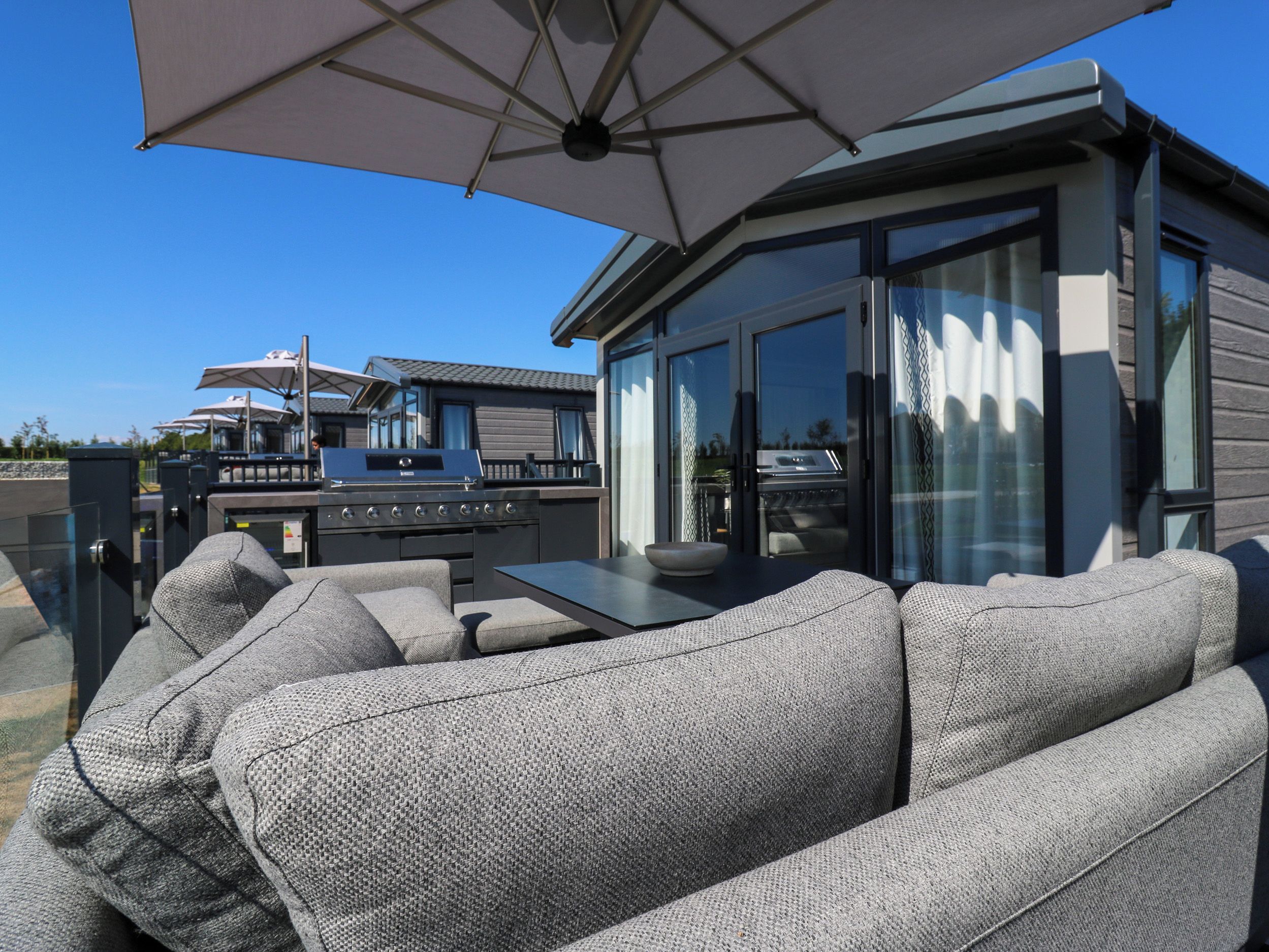 An outdoor patio with a dining table, grey upholstered sofa, and a barbecue grill.