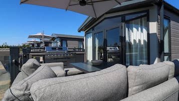 An outdoor patio with a dining table, grey upholstered sofa, and a barbecue grill.