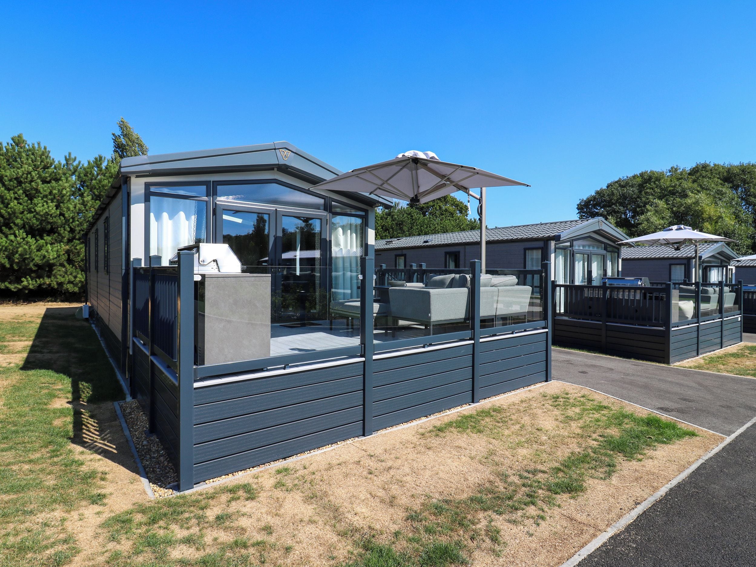 A modern mobile home with a glass enclosure, a patio area, and a covered outdoor seating space.