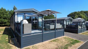 A modern mobile home with a glass enclosure, a patio area, and a covered outdoor seating space.