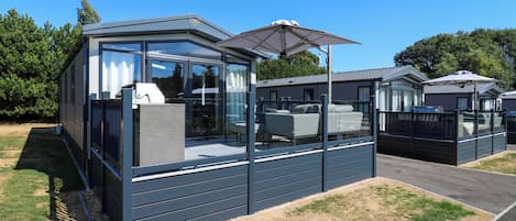 A modern mobile home with a glass enclosure, a patio area, and a covered outdoor seating space.
