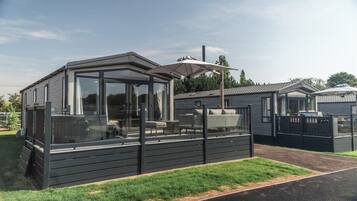 A modern, single-story mobile home with a glass-enclosed patio area, a built-in grill, and a covered outdoor seating area.