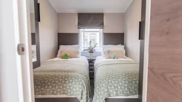 A narrow room with two beds, a window with curtains, and a small table with a vase of flowers.