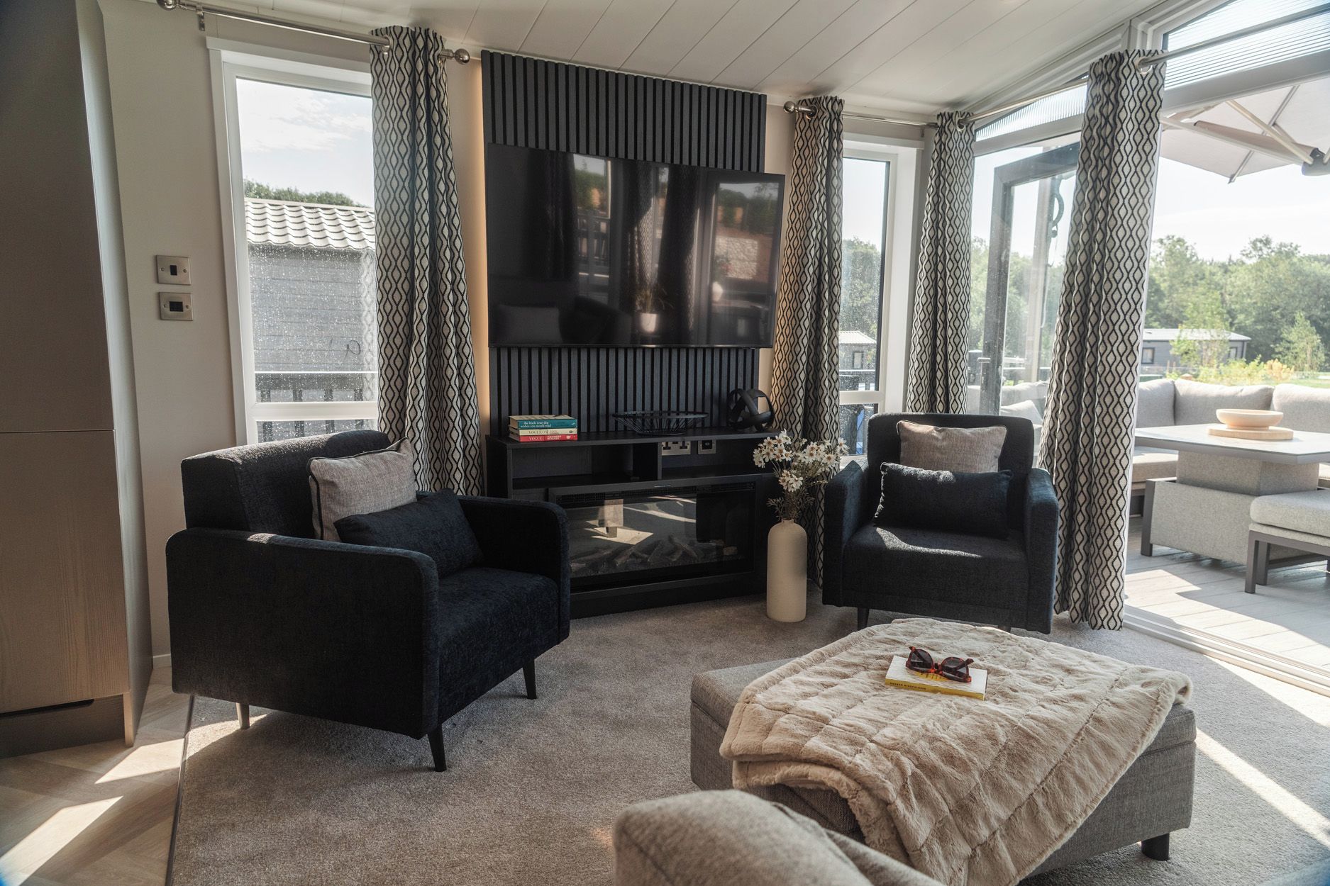 A modern living room with a flat-screen TV, two armchairs, a coffee table, and a fireplace.