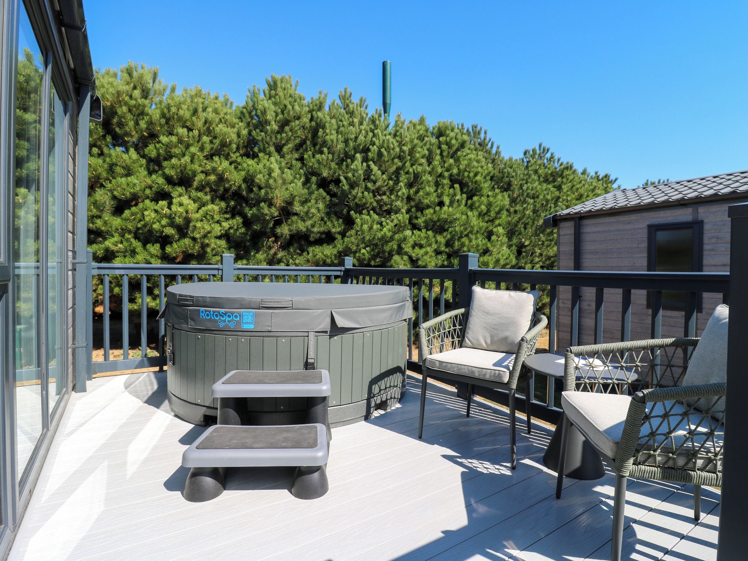 Una terraza con mobiliario exterior, un jacuzzi y vistas a un bosque.