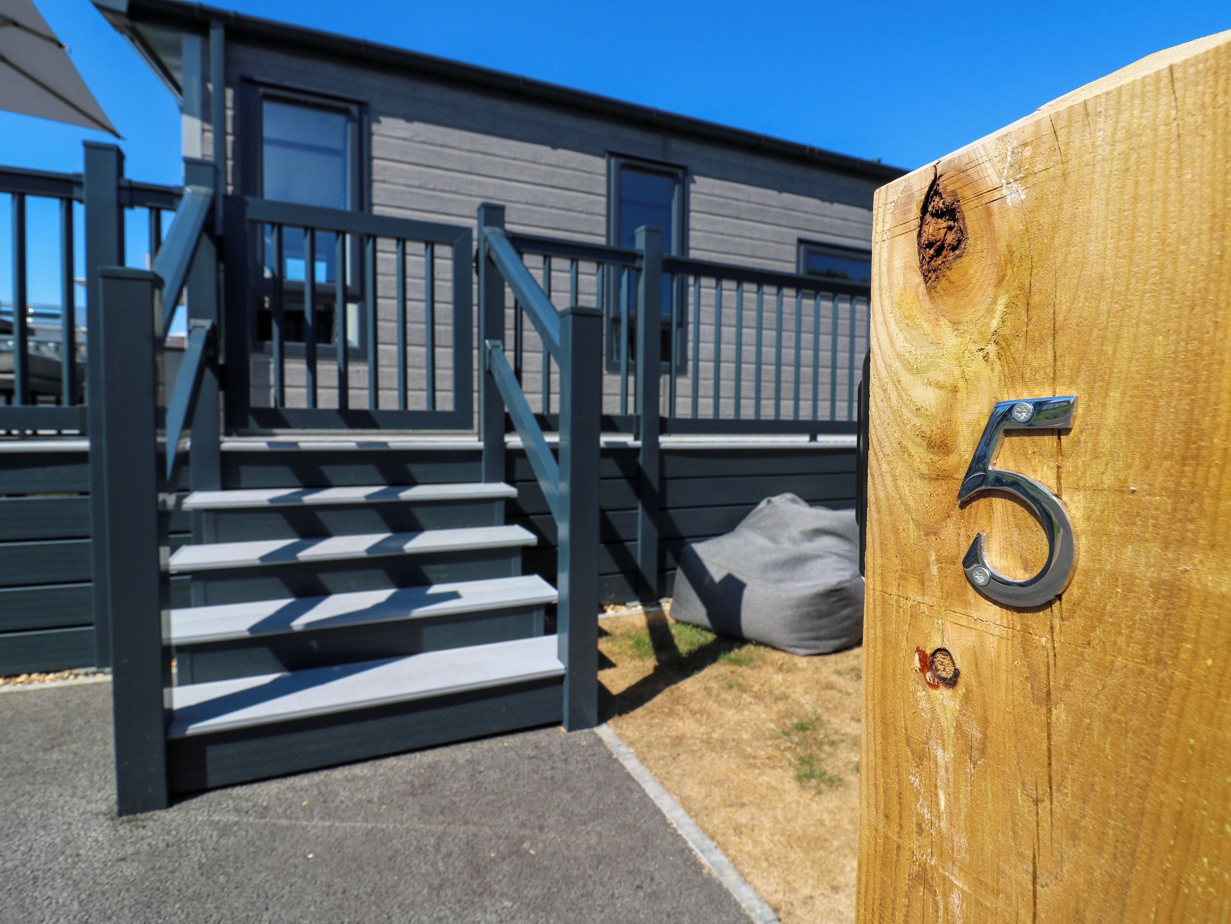 Een houten poort met het nummer 5, een trap die naar een gebouw leidt, en een heldere blauwe lucht.