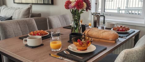 A dining table with breakfast items, a vase with flowers, and a view of the outside.