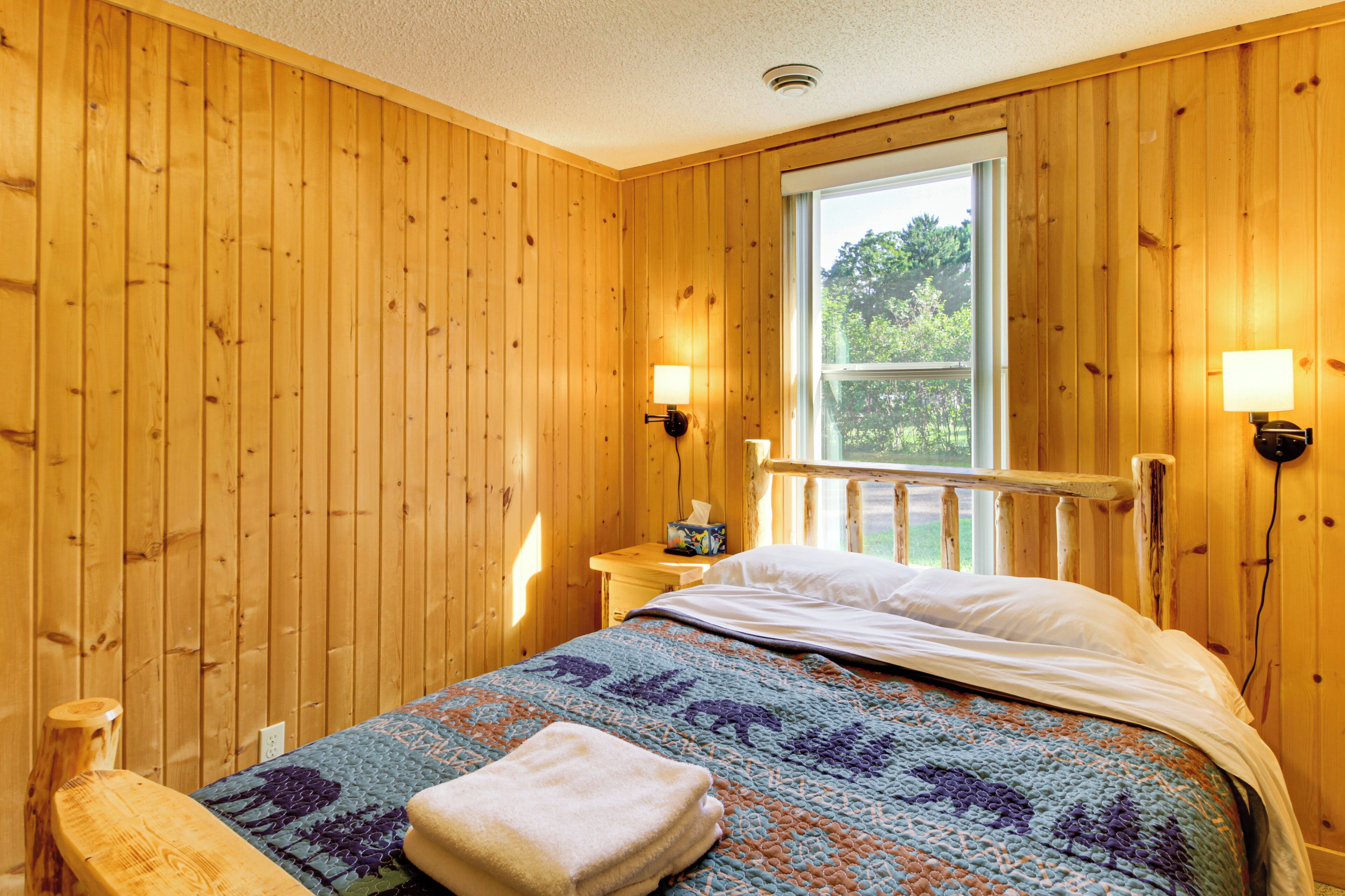 Una habitación con paneles de madera, una cama, un ventanal y dos lámparas fijadas a la pared.
