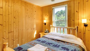 Una habitación con paneles de madera, una cama, un ventanal y dos lámparas fijadas a la pared.