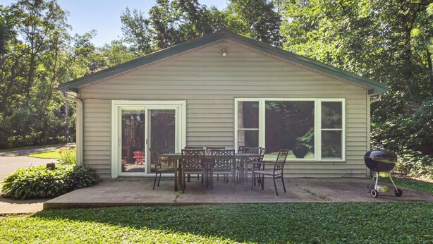 A small single-story house with a patio, a table with chairs, and a grill.
