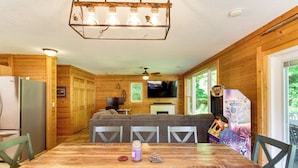 A wooden interior with a dining table, chairs, a television, and a fireplace.