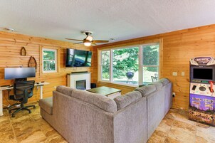 Una habitación acogedora con sofá, televisión de pantalla plana, chimenea y un amplio ventanal con vistas al verdor.