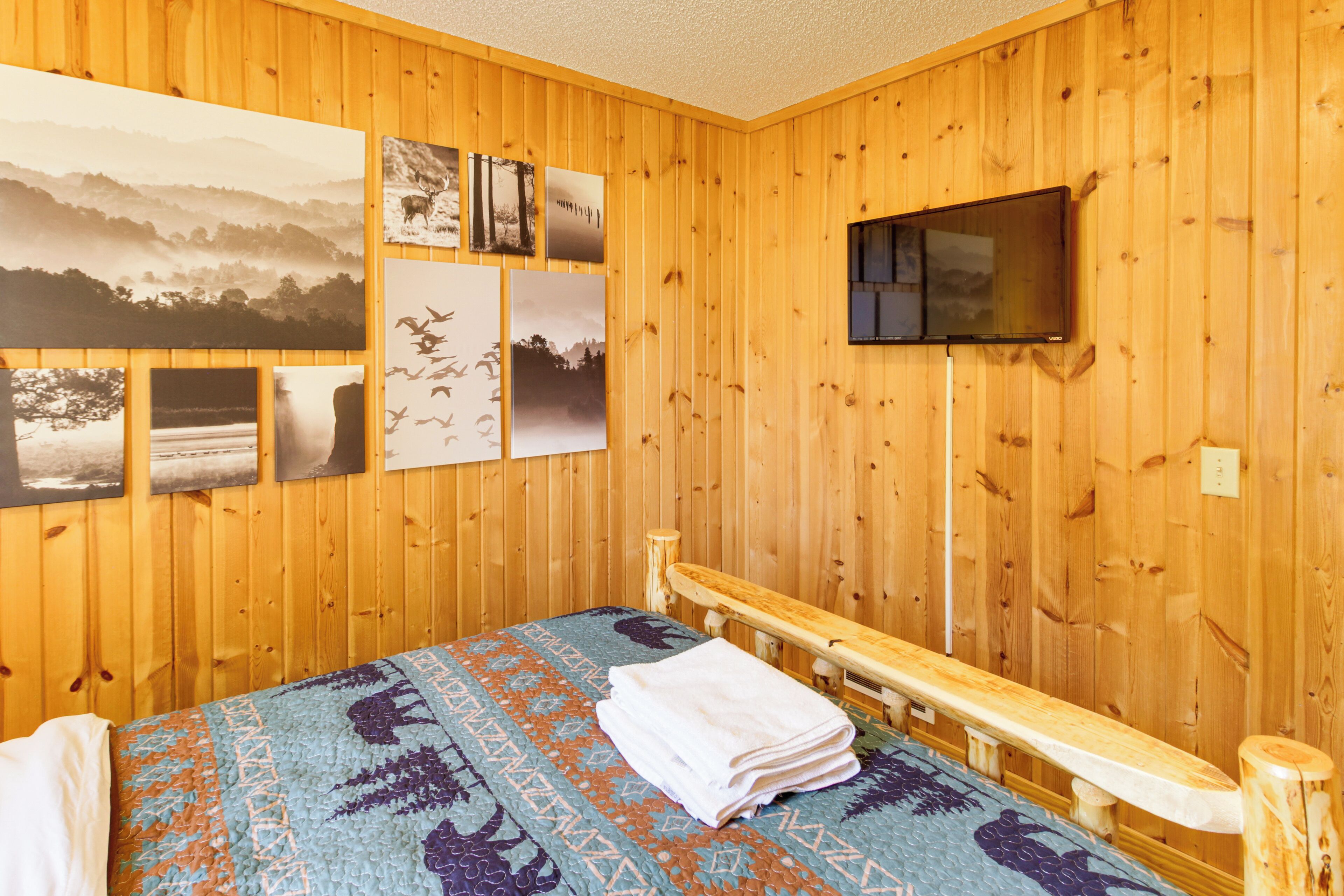 A wooden-paneled room with a bed, a TV mounted on the wall, and several framed pictures.