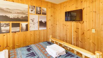 A wooden-paneled room with a bed, a TV mounted on the wall, and several framed pictures.