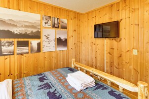 Una habitación con paneles de madera, una cama, un televisor montado en la pared y varias fotografías enmarcadas.