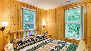 A wooden cabin room with a bed, two windows, and a nightstand.