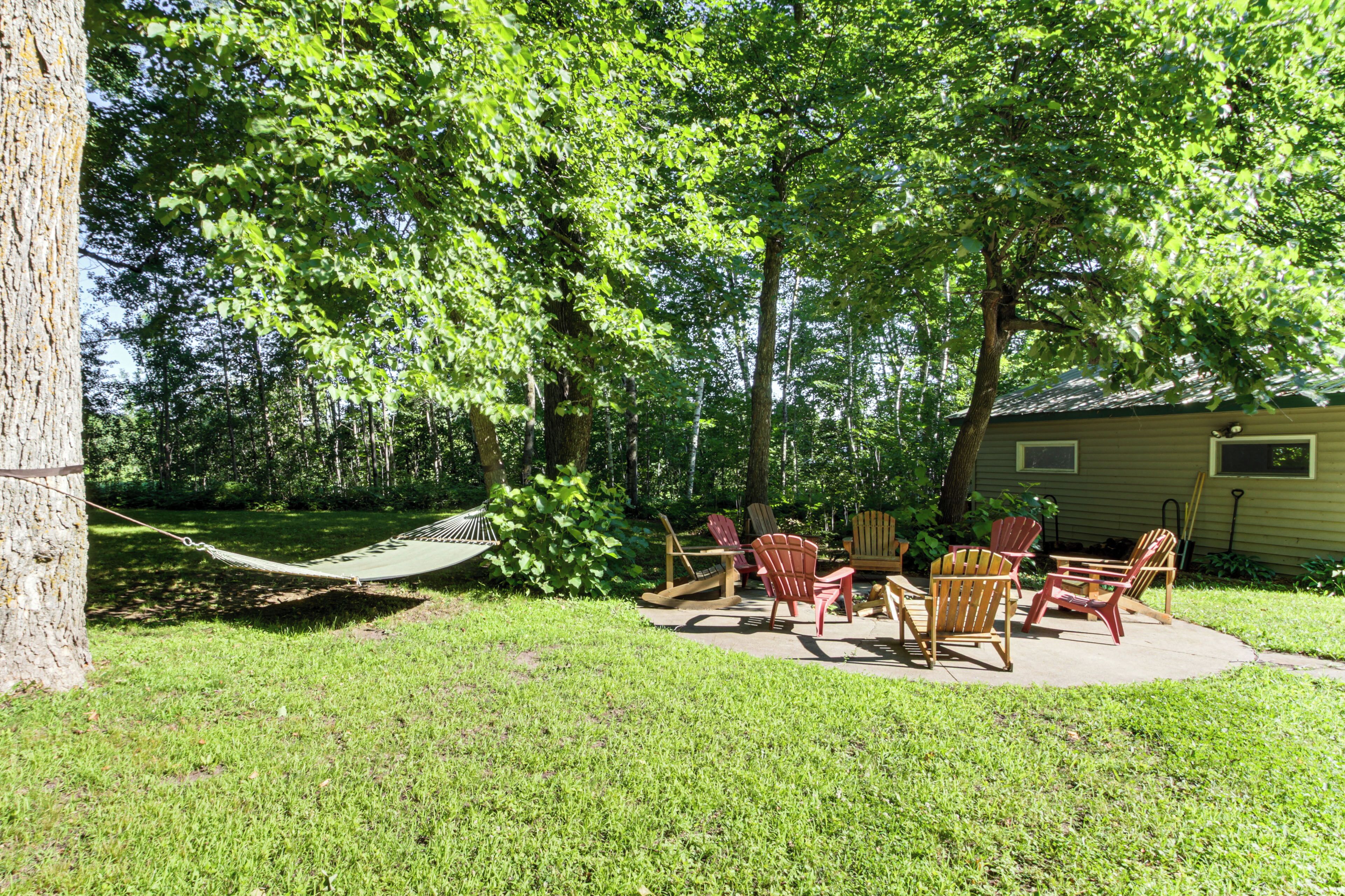 A backyard with a hammock, several Adirondack chairs, and a small patio area.