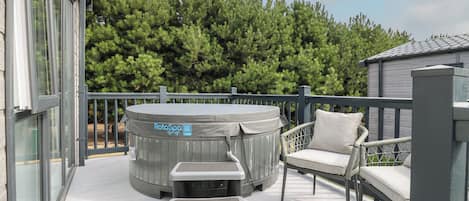 A rooftop deck with a hot tub, a cushioned chair, and a small table.